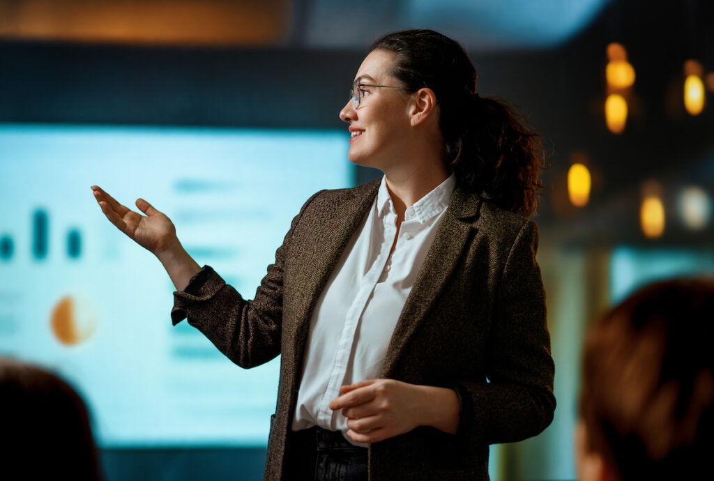A young professional giving a presentation in front of a large projection screen.